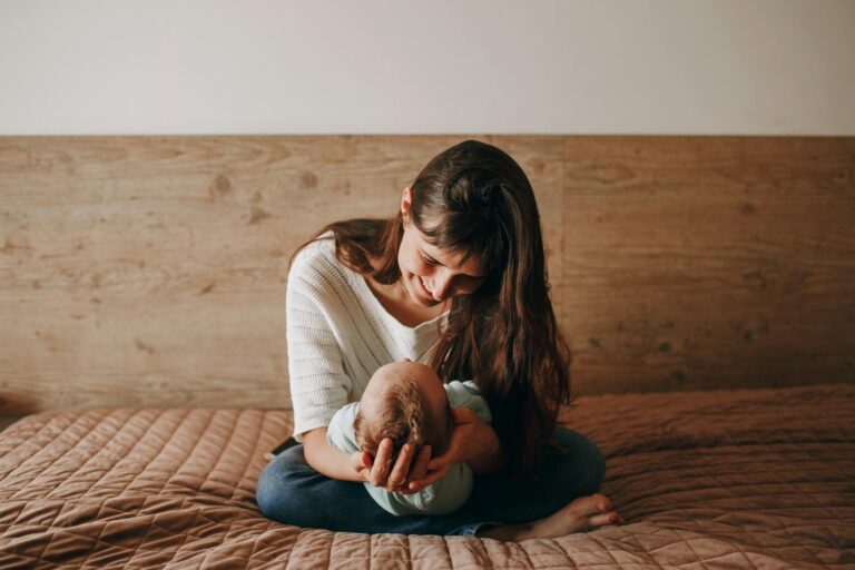Epilepsie und Kinderwunsch: Was Sie beachten sollten A heartwarming scene of a mother gently holding her baby on a bed, captured in a cozy bedroom setting.