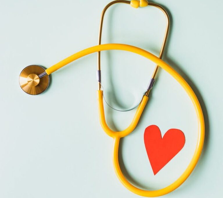 Yellow stethoscope arranged with a red heart cutout on a light green background, symbolizing heart health.