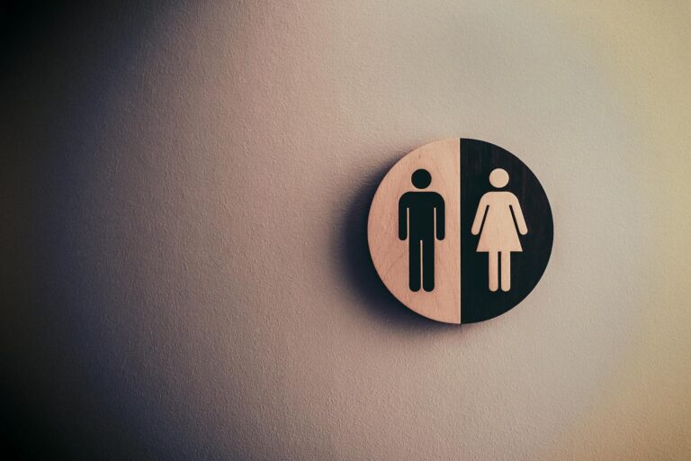 Rheumatoide Arthritis: Geschlechterunterschiede verstehen Minimalist gender neutral restroom sign with male and female symbols on textured wall.
