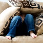 A child crouched under cushions on a couch, conveying a sense of playfulness or fear.