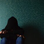 A person sits alone in a hoodie, conveying a sense of solitude and introspection.