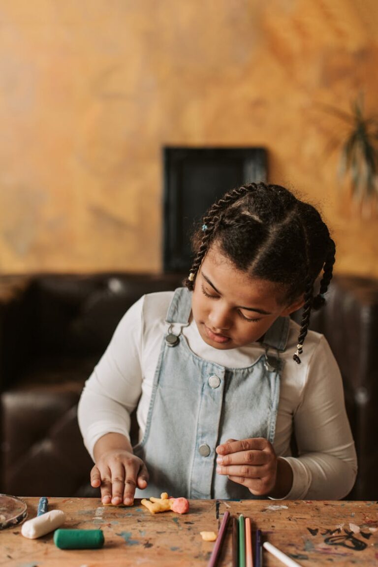 Child focusing on handmade crafts using colorful clay at a wooden table indoors.