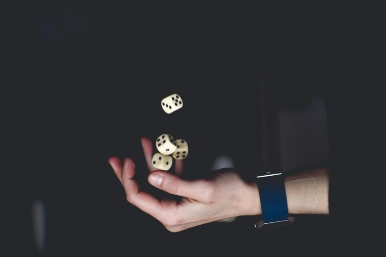 Pathologisches Glücksspiel A close-up of a hand tossing several dice against a dark background, symbolizing chance and luck.