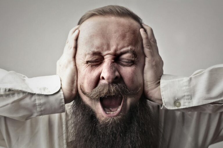 Zwanghafte Persönlichkeitsstörung Portrait of a man with facial hair, covering his ears and screaming, expressing stress or frustration.