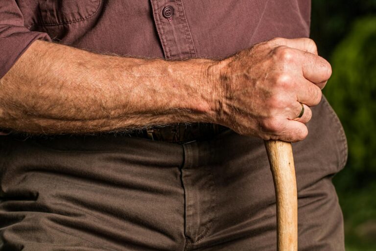 Spät einsetzende Alzheimer-Krankheit Close-up of a senior adult's hand gripping a wooden walking cane outdoors, symbolizing support and aging.