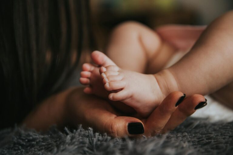 Postpartale psychische Erkrankungen Close-up of a mother's hand gently holding her baby's tiny feet, symbolizing warmth and affection.