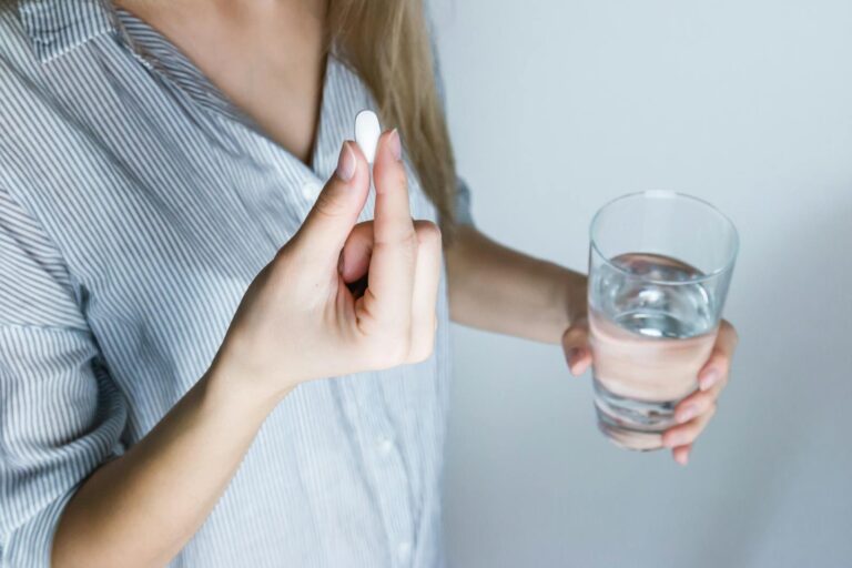 Hyperkaliämie Close-up of a woman holding a pill and a glass of water, ready to take medication.