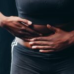 Close-up of a person pressing hands on abdomen, indicating discomfort or pain, against a black background.