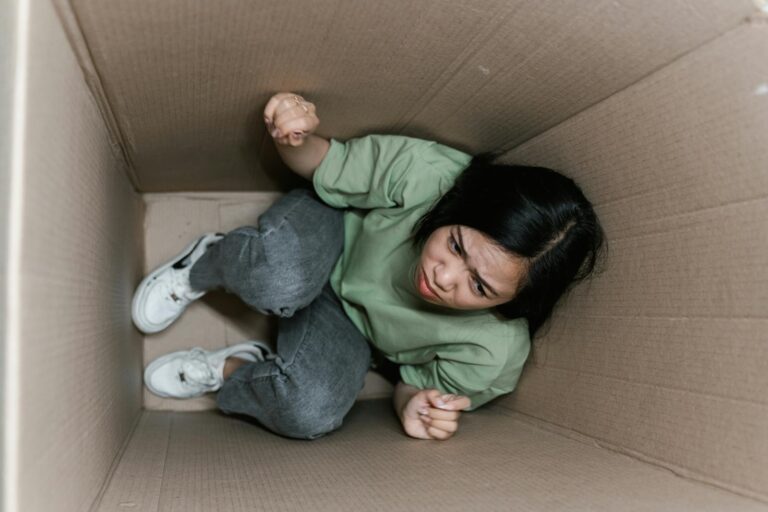 Agoraphobie A woman feeling trapped and anxious inside a small cardboard box, symbolizing claustrophobia.