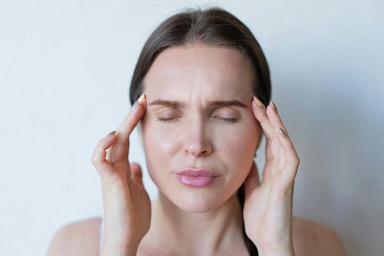 Migräne mit Aura Close-up of a woman with closed eyes holding her temples, showing signs of a migraine or headache.
