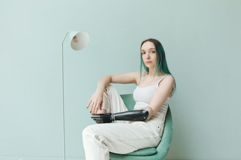 Phantomschmerz Portrait of a woman with prosthetic arm seated in a stylish interior, wearing a white tank top.