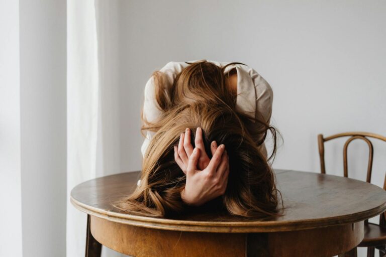 Einfache Schizophrenie A woman showing despair with her head down on a table, indicating stress.