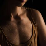 Close-up of a woman's wet skin with water droplets, set against a dark background.