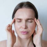 Close-up of a woman with closed eyes holding her temples, showing signs of a migraine or headache.