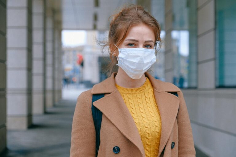 Durch Retroviren verursachte Infektionen Young woman in a coat and mask stands outdoors, promoting health and safety measures.