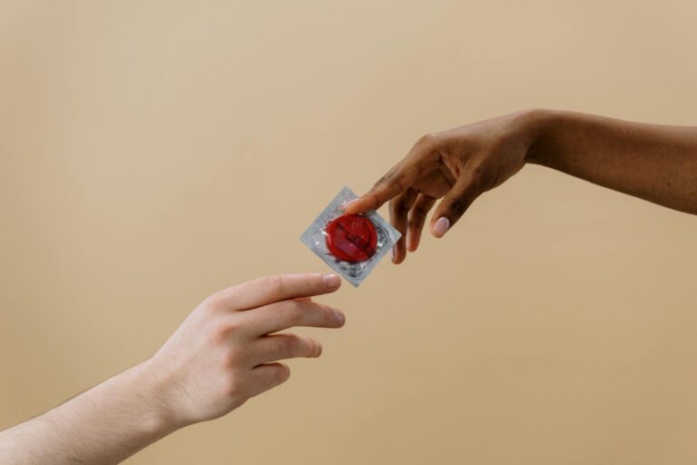 Frühe Syphilis A close-up of two diverse hands exchanging a red condom, promoting safe sex and contraception.