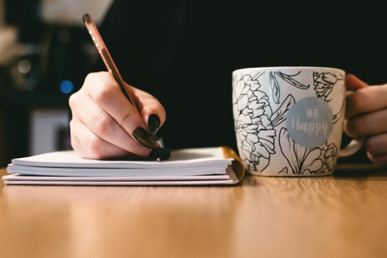 isolierte Rechtschreibschwäche Person writing in a notebook with a floral ceramic mug on a wooden desk.
