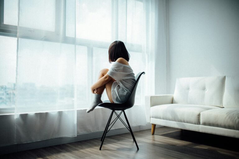 Dysthymie woman sitting on black chair in front of glass-panel window with white curtains