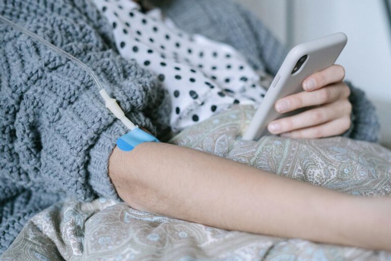 A woman receiving intravenous therapy for cancer treatment while using her phone, symbolizing connection and hope.