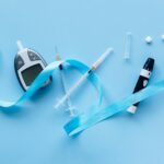 Flat lay of diabetes management tools with blue ribbon symbolizing awareness on a light blue background.