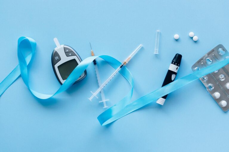 Flat lay of diabetes management tools with blue ribbon symbolizing awareness on a light blue background.