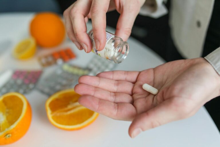 Megavitamin-B6-Syndrom Close-up of a person taking a vitamin capsule with citrus fruit and medication on a table.